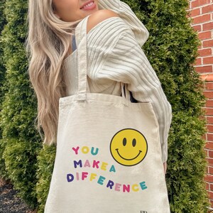 May include: A white canvas tote bag with the text "YOU MAKE A DIFFERENCE" in colorful letters and a yellow smiley face.