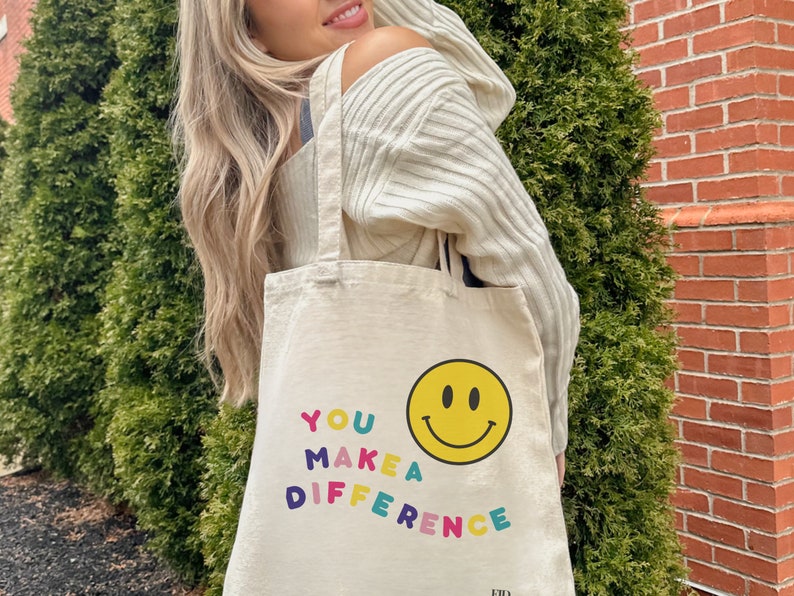 May include: A white canvas tote bag with the text "YOU MAKE A DIFFERENCE" in colorful letters and a yellow smiley face.