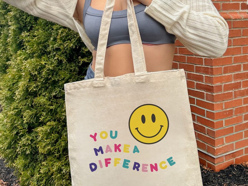 May include: A beige canvas tote bag with the text "YOU MAKE A DIFFERENCE" in colorful letters and a yellow smiley face.