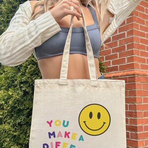 May include: A white canvas tote bag with the text "YOU MAKE A DIFF" in colorful letters and a yellow smiley face.