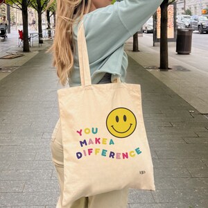 May include: A beige canvas tote bag with a yellow smiley face and the text "YOU MAKE A DIFFERENCE" in colorful letters.