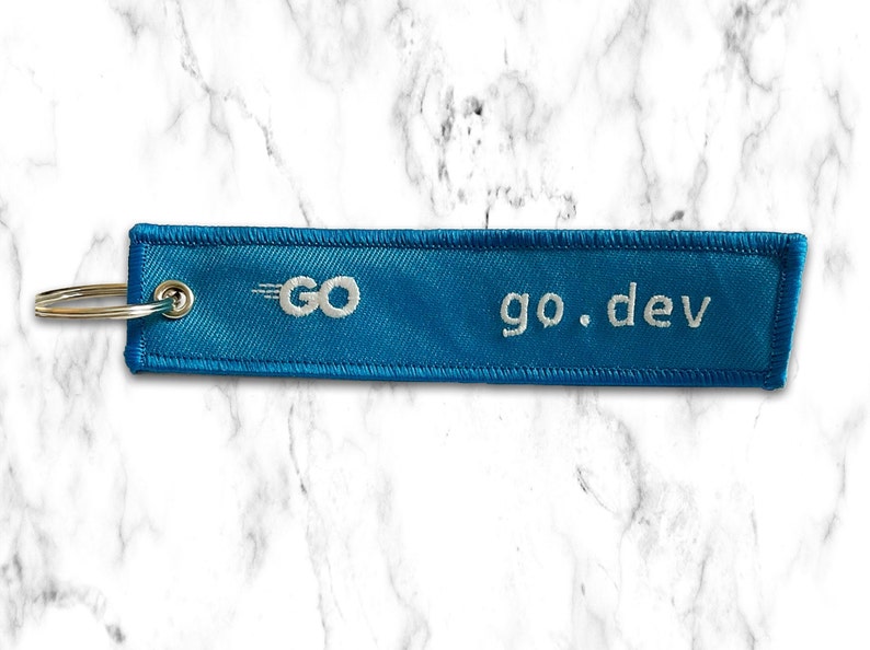 K&ouml;nnte beinhalten: Ein blauer Stoffschl&uuml;sselanh&auml;nger mit wei&szlig;en N&auml;hten und dem Text "go.dev" sowie einem wei&szlig;en Logo mit dem Text "GO" und einem wei&szlig;en stilisierten Pfeil.