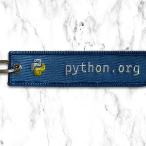K&ouml;nnte beinhalten: Ein blauer Schl&uuml;sselanh&auml;nger mit einem gelben und wei&szlig;en Python-Logo und dem Text "python.org" darauf gestickt.