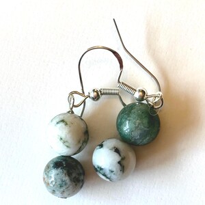 May include: A pair of earrings featuring four round beads in shades of white, green, and gray. The beads are attached to silver-colored ear wires. The earrings have a natural, organic appearance.