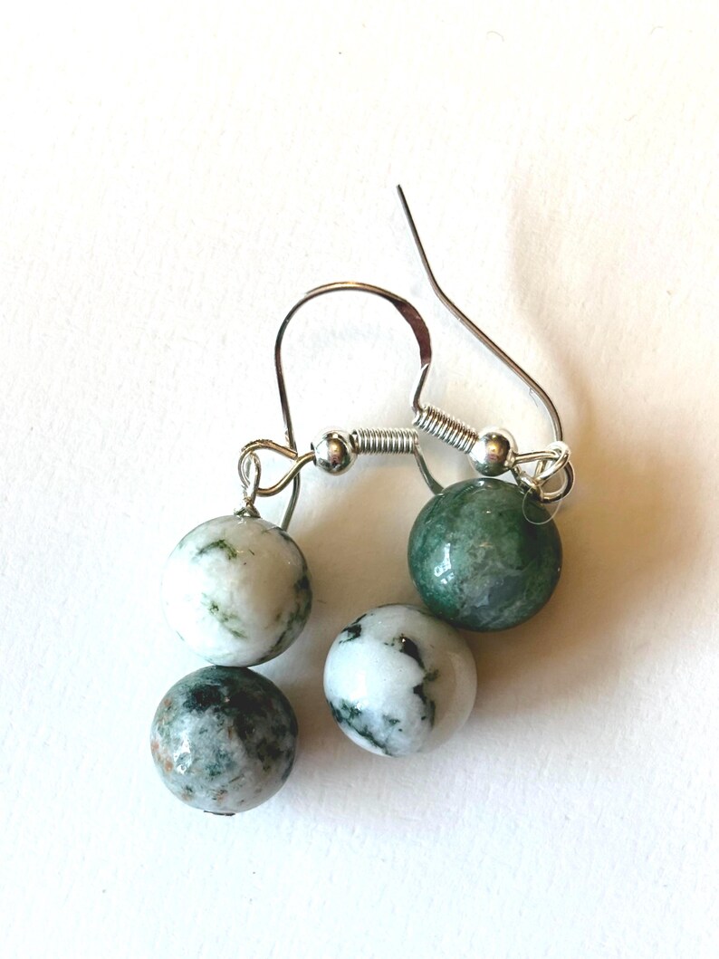 May include: A pair of earrings featuring four round beads in shades of white, green, and gray. The beads are attached to silver-colored ear wires. The earrings have a natural, organic appearance.
