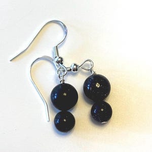 May include: A pair of dangle earrings featuring dark blue, spherical beads with a silver-colored hook. The beads have a speckled appearance, and each earring has two beads of different sizes.