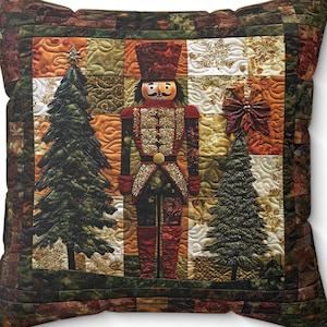May include: Square decorative pillow with a quilted design featuring a nutcracker soldier, two Christmas trees, and a star. The pillow has a patchwork pattern with shades of green, brown, and gold. The nutcracker is dressed in red and gold.