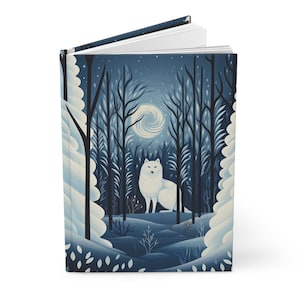 May include: Hardcover journal featuring a winter forest scene with a white arctic fox. The cover art depicts a moonlit forest with snow-covered trees and a swirling moon. The journal is open, revealing blank white pages.