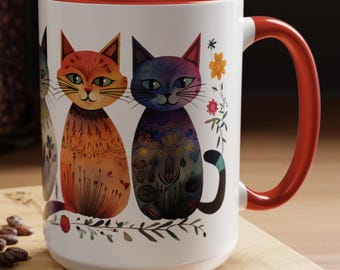 May include: White ceramic coffee mug with a red rim and handle. The mug features a colorful illustration of three cats with floral designs.