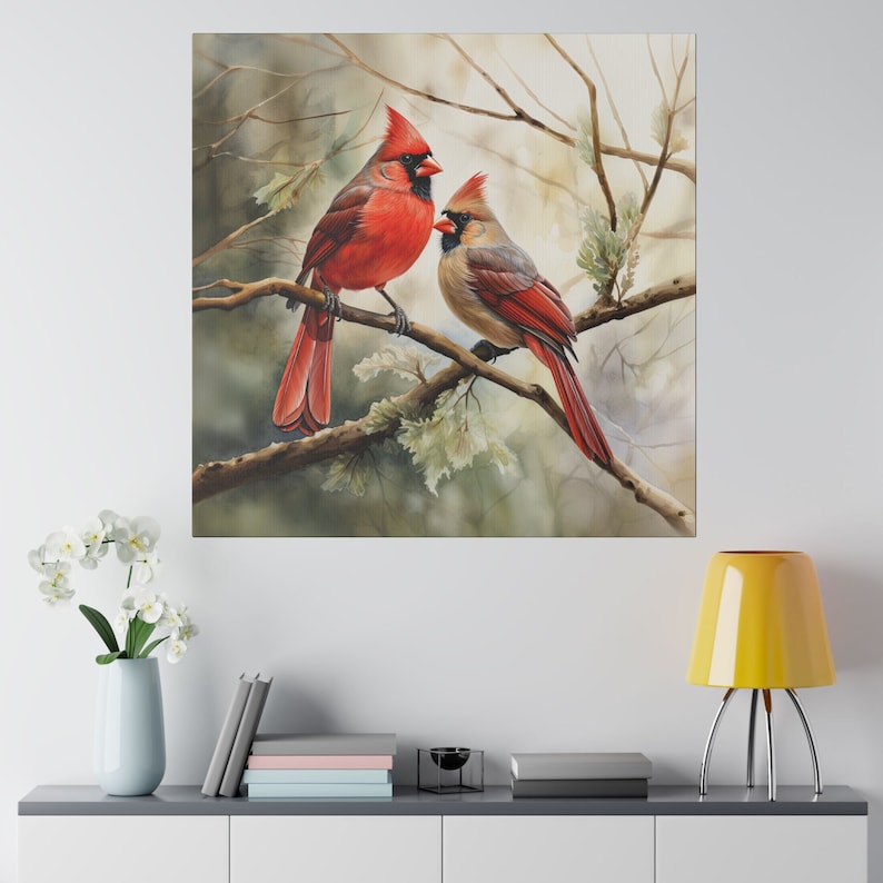 Op de afbeelding: Een schilderij met twee rode kardinaals, die op een tak zitten. De mannelijke kardinaal is links en de vrouwelijke kardinaal is rechts. De kardinaals zijn omringd door groene bladeren en takken.
