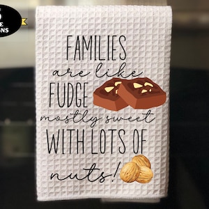 May include: White kitchen towel with the text "Families are like fudge mostly sweet with lots of nuts!" and a graphic of two pieces of fudge with nuts on top.