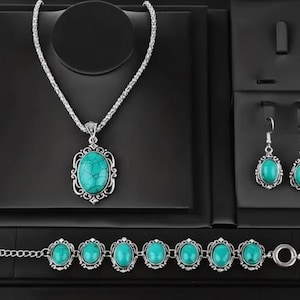May include: A jewellery set comprising a silver necklace, bracelet, and earrings. Each item features an oval turquoise stone within a decorative silver frame. The set is presented on a black velvet display.