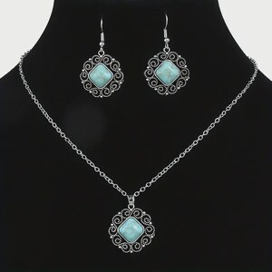 K&ouml;nnte beinhalten: Ein silberfarbenes Schmuckset mit Halskette und passenden Ohrringen. Jedes St&uuml;ck hat einen quadratischen, hellblauen Stein, der in einem dekorativen, durchbrochenen Rahmen gefasst ist. Die Halskette hat eine zarte Kette.