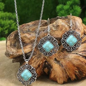 K&ouml;nnte beinhalten: Ein silberfarbenes Schmuckset mit Halskette und Ohrringen. Jedes St&uuml;ck hat einen quadratischen, hellblauen Stein, der in einen dekorativen, durchbrochenen Rahmen gefasst ist. Die Halskette hat eine zarte Kette, und die Ohrringe haben Hakenverschl&uuml;sse.