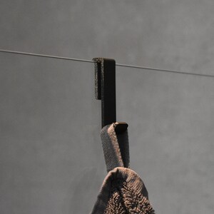 May include: A black metal hook mounted on a wall with a gray towel hanging from it.