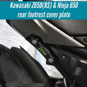 Puede incluir: Placa de cubierta de reposapiés trasero de motocicleta negra con un logotipo "Z650" verde y negro.