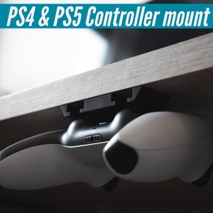 Könnte beinhalten: Eine schwarze Plastikhalterung, die an der Unterseite eines Holztisches befestigt ist, hält einen weißen PS5-Controller.