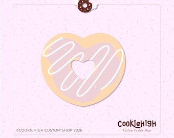 Op de afbeelding: Een hartvormige koek met een hartvormige uitsparing, versierd met roze glazuur en witte glazuurkrullen. Een kleine donut met engelen vleugels en een halo zit boven de koek. De tekst "CookieHigh Custom Shop 2026" is inbegrepen.