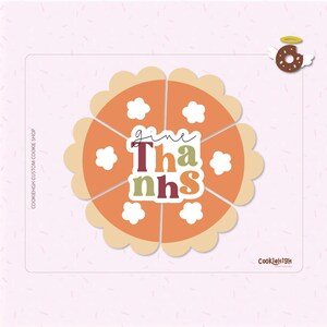 May include: A Thanksgiving-themed cookie cutter in the shape of a pie, divided into six slices. The pie is orange with a tan crust and white flower-shaped accents. The words "give Thanks" are in the center.