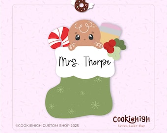 Op de afbeelding: Een kerstkoekjesvorm in de vorm van een kous met een peperkoeken mannetje. De groene kous heeft sneeuwvlokken en de naam "Mrs. Thorpe". Een zuurstok, bessen en een donut met vleugels zijn ook inbegrepen.