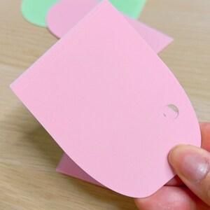 May include: A pink plastic scraper with a hole in the handle. The scraper is used for spreading frosting or icing on cakes and cookies.