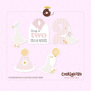 Può includere: Una collezione di decorazioni di compleanno a tema oca, rosa chiaro e bianco. Include una ciambella con ali d'angelo, il numero due, un cappello da festa e un'oca che tiene in mano un palloncino. È presente anche il testo "Emery is two silly goose".