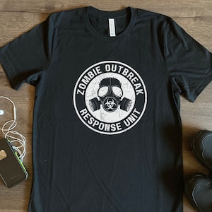 Könnte beinhalten: Schwarzes T-Shirt mit einer weißen Grafik einer Gasmaske mit dem Text "Zombie Outbreak Response Unit" drumherum.