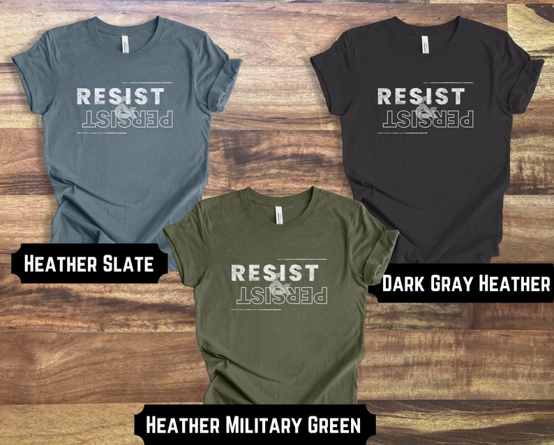May include: Three t-shirts with the text "Resist & Persist" in white lettering on a dark background. The t-shirts are in the colors heather slate, dark gray heather, and heather military green.