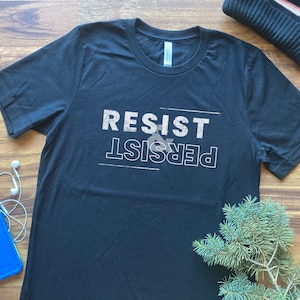 May include: Black t-shirt with white text that reads "Resist & Persist".