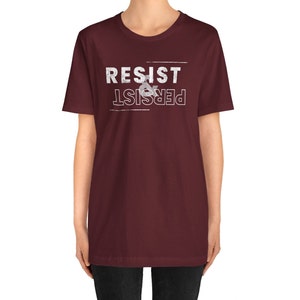 May include: A maroon t-shirt with white text that reads "Resist & Persist" in a distressed font.