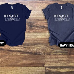 May include: Two t-shirts with the text "Resist & Persist" in white lettering on a navy blue and navy heather background.