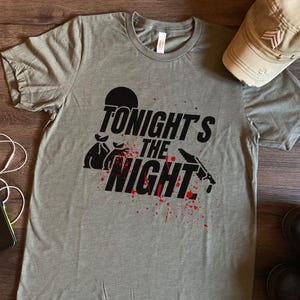 Könnte beinhalten: Ein graues T-Shirt mit dem Text "Tonight's the Night" in Schwarz mit einer Grafik einer Geldbörse und einer blutigen Hand, die ein Messer hält.