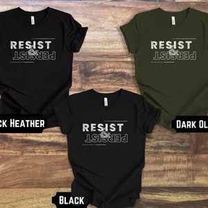 May include: Three t-shirts with the text "Resist & Persist" in white on a black, dark olive, and black heather background.