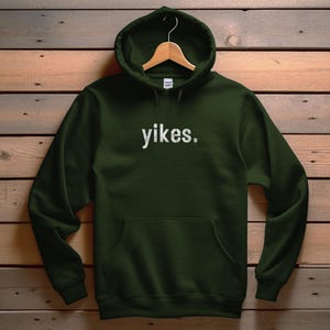 Puede incluir: Una sudadera con capucha de color verde oscuro con la palabra "yikes." impresa en blanco en la parte delantera.