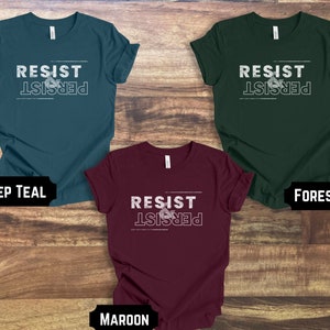 May include: Three t-shirts in different colors: deep teal, forest green, and maroon. Each shirt has the text "RESIST & PERSIST" printed on the front in white.