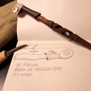 Peut inclure: Une canne de marche en bois avec un motif en spirale à l'extrémité. La canne est en merbau et en ébène du Brésil et mesure 13,5 pouces de long. Le texte "THE MARINER: MERBAU AND BRAZILIAN EBONY 13.5 INCHES" est écrit sur un morceau de papier.