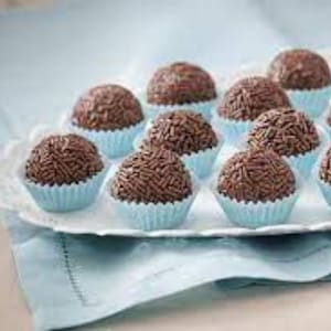 May include: A close-up of a platter of chocolate truffles, each individually wrapped in a light blue paper cup. The truffles are arranged in a circular pattern, with the tops of the truffles visible.