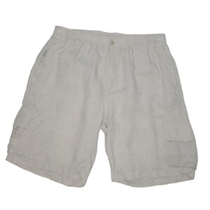 May include: Light beige linen shorts with two large pockets on the sides. The shorts have an elastic waistband and a button closure.