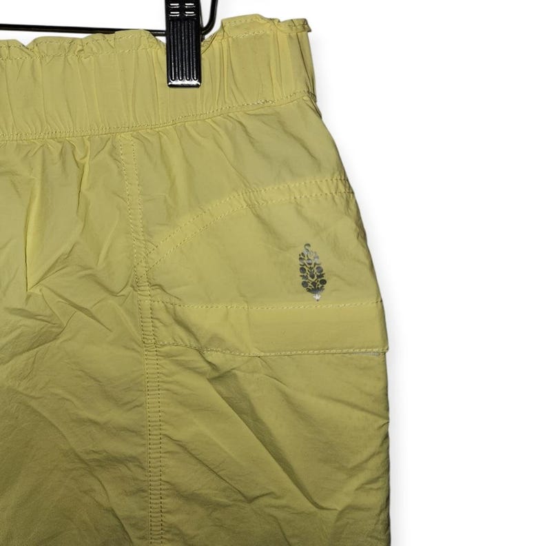 May include: Pale yellow athletic shorts with an elasticated waistband and a small pocket. The shorts have a subtle sheen and a small logo on the pocket. The fabric appears lightweight, suitable for exercise or casual wear.