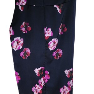May include: A navy blue skirt with a floral pattern. The skirt features a series of pink and red flowers scattered across the fabric. The skirt is hanging from a metal hanger.