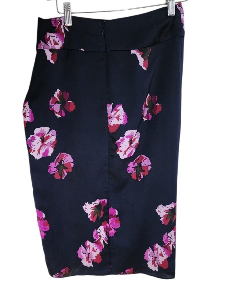 May include: A navy blue skirt with a floral pattern. The skirt features a series of pink and red flowers scattered across the fabric. The skirt is hanging from a metal hanger.