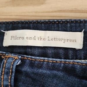 May include: A distressed white wooden sign displaying the word "Welcome" in a handwritten font. A small heart decoration is attached. The sign has a rustic appearance, with a blurred wooden background.