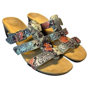 以下が含まれることがあります： グレー、オレンジ、ベージュの色合いのヘビ柄のオープントゥサンダル。調節可能なバックルが付いた複数のストラップとウェッジヒールが付いています。フットベッドはタン色です。