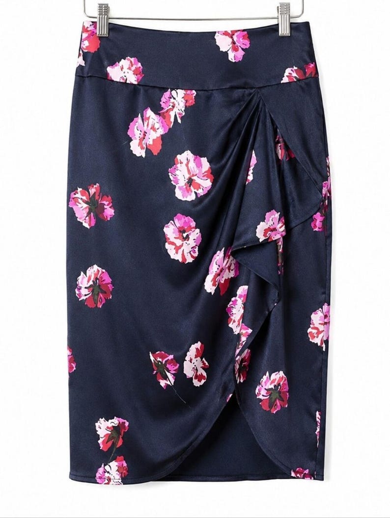 May include: A navy blue pencil skirt with a floral pattern. The skirt features a wrap design with a ruffled edge. The flowers are pink and red, and the skirt is made of a shiny fabric.