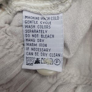 May include: Close-up of a clothing care label with the text "MACHINE WASH COLD, GENTLE CYCLE, WASH COLORS SEPARATELY, DO NOT BLEACH, HANG DRY, WARM IRON IF NECESSARY, CAN BE DRY CLEAN". The label is white with black text.