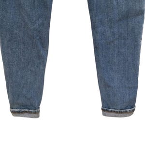 May include: Close-up of the lower portion of light blue denim jeans. The jeans have a classic, faded wash and are cuffed at the ankles. The fabric shows subtle texture and wear, typical of denim.