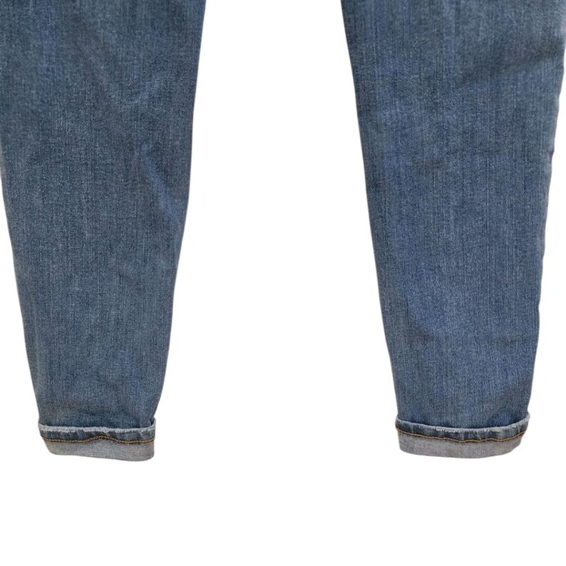 May include: Close-up of the lower portion of light blue denim jeans. The jeans have a classic, faded wash and are cuffed at the ankles. The fabric shows subtle texture and wear, typical of denim.