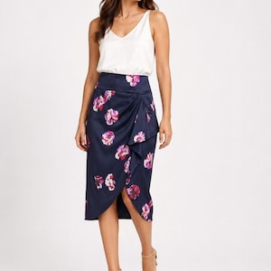 May include: A woman wearing a white V-neck tank top and a navy blue wrap skirt with a floral pattern in pink and purple. The skirt falls to the knees. She is wearing nude heels.