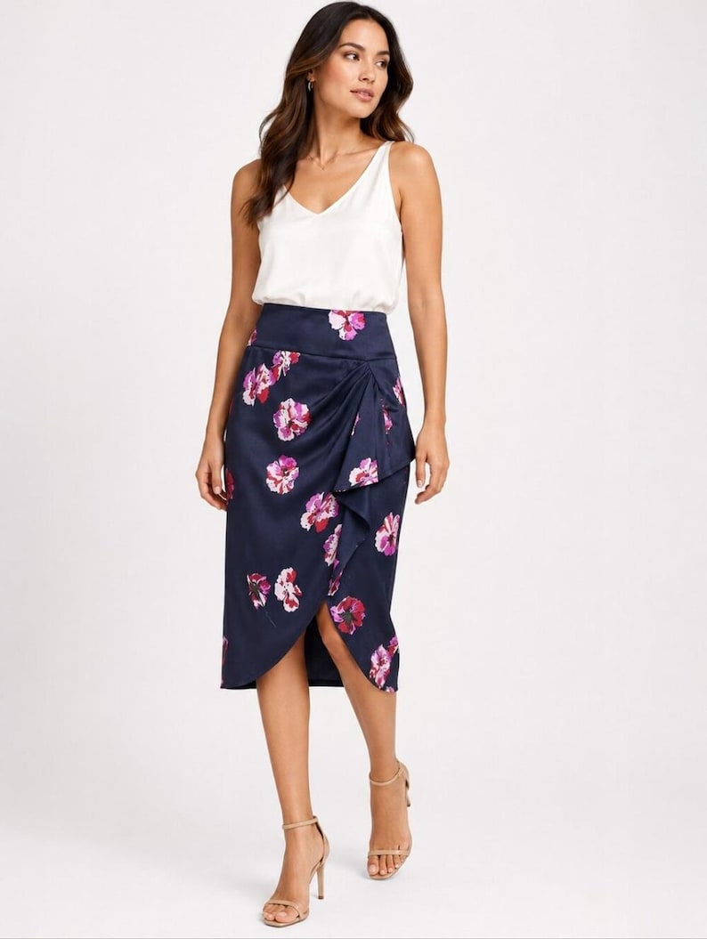 May include: A woman wearing a white V-neck tank top and a navy blue wrap skirt with a floral pattern in pink and purple. The skirt falls to the knees. She is wearing nude heels.