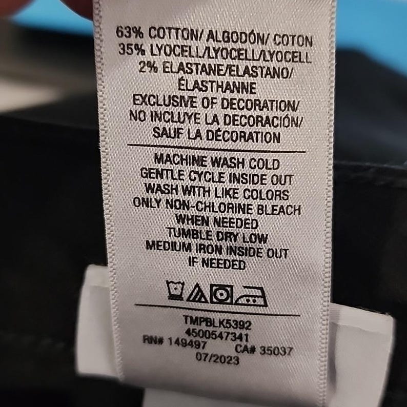 May include: A white clothing tag with black text detailing fabric composition: 63% cotton, 35% lyocell, and 2% elastane. Washing instructions include machine wash cold, gentle cycle, and tumble dry low. The tag also includes a product code and date.